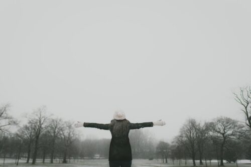 A woman spreading her arms in the park on a foggy winter day