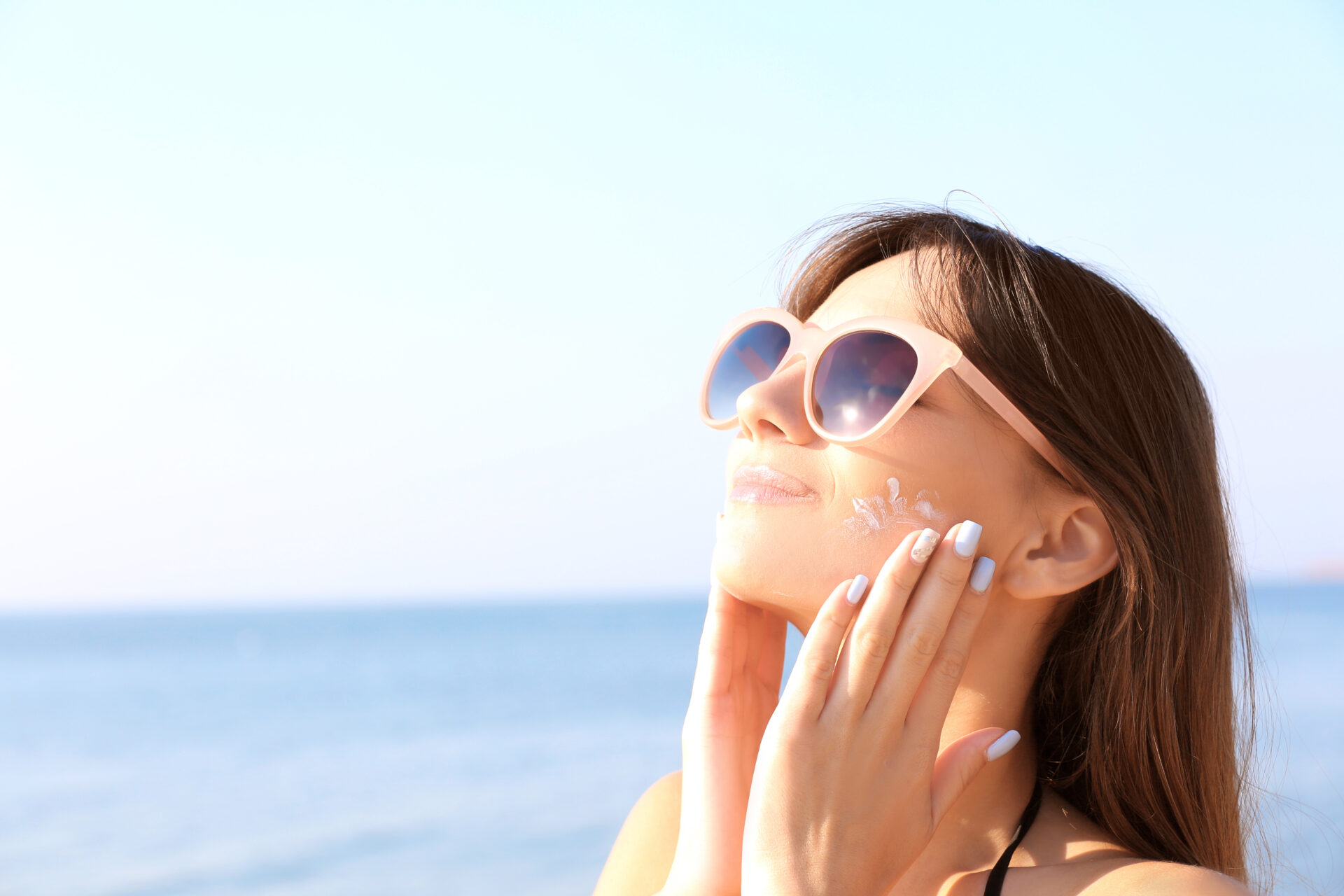 A woman applying sunscreen by the sea